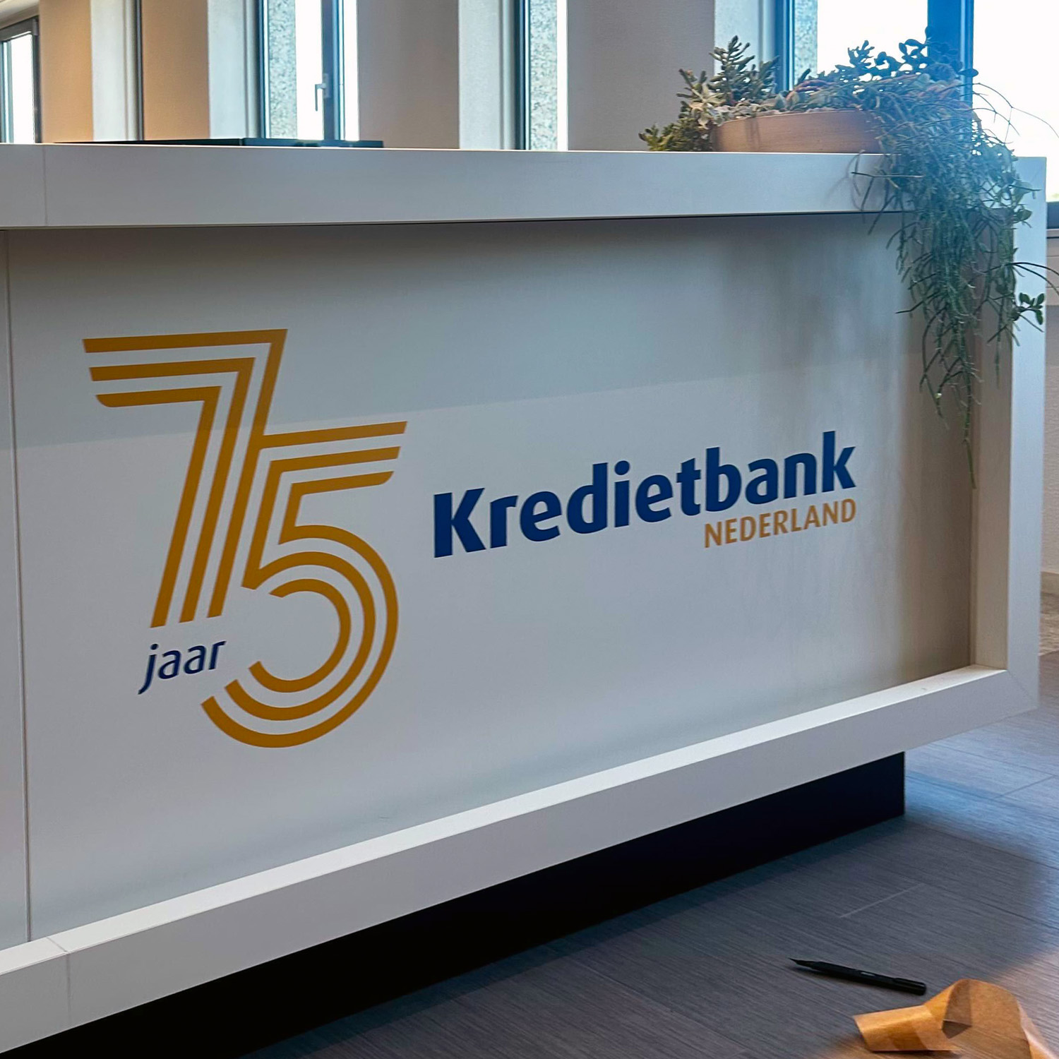 Jubileumstickers met logo van Kredietbank Nederland op een witte ontvangstbalie
