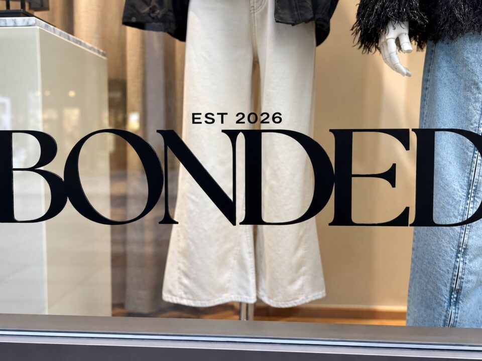 Close-up van de zwarte BONDED-raambelettering met EST 2026 op het etalageglas