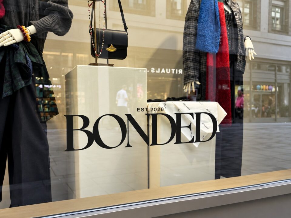 Zwarte BONDED-raambelettering op de etalageruit, met kledingpresentatie op de achtergrond