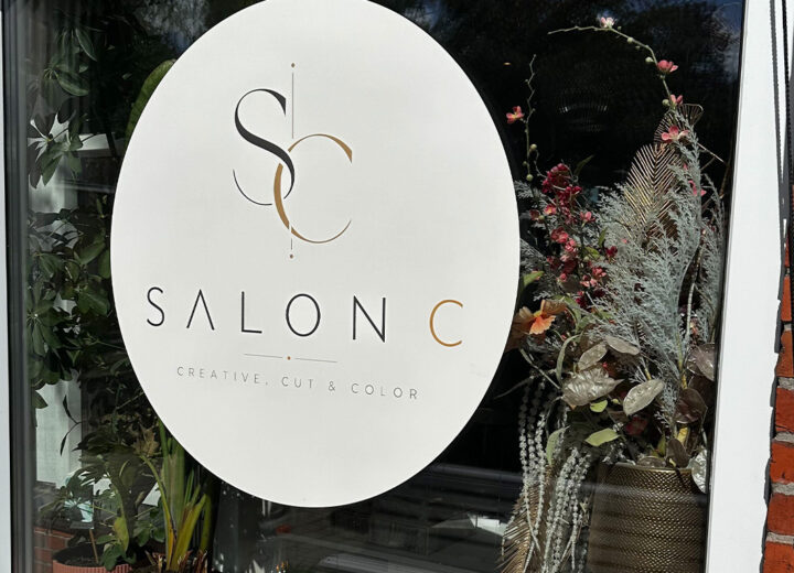 Ronde witte raamsticker met bedrijfslogo op de etalageruit van een kapsalon